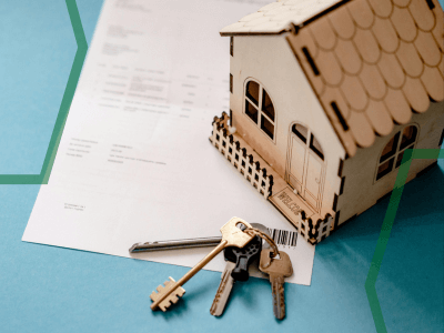 An image showing a wooden house model, a set of keys, and a legal document on a table